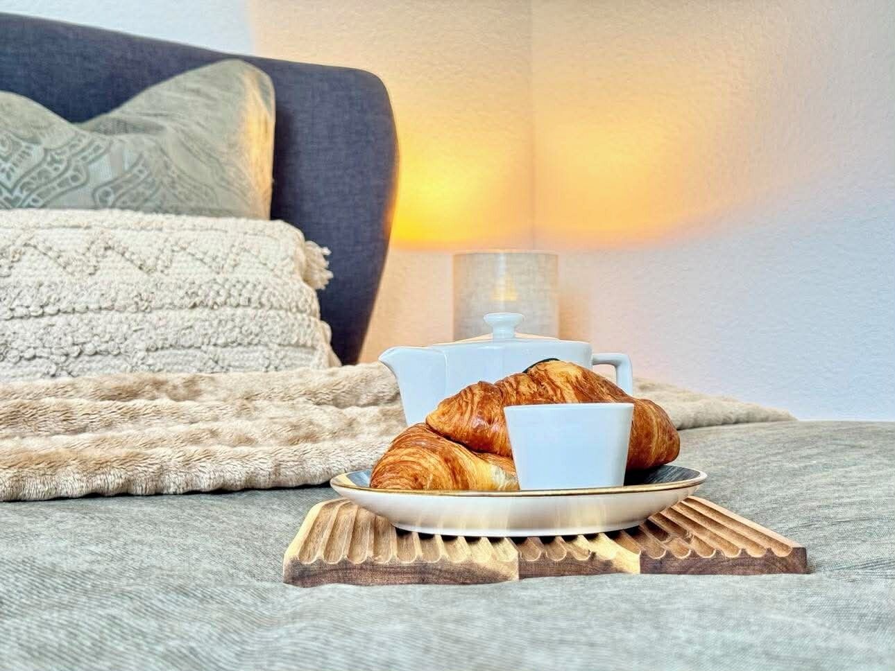A cozy room with a bed, a bedside lamp, and a plate with croissants and a cup.