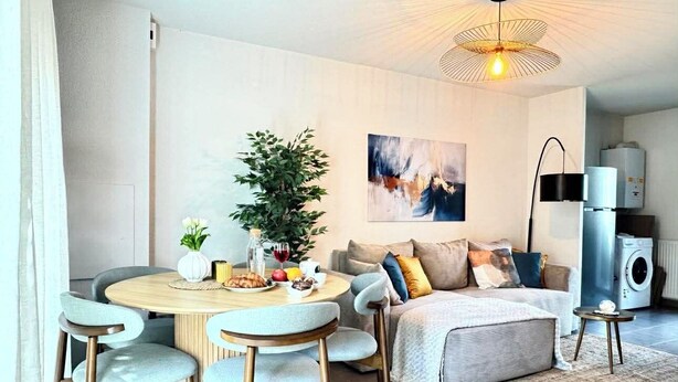 Un salon moderne avec une table à manger ronde, un canapé, un lit, une plante en pot et un luminaire suspendu au plafond.