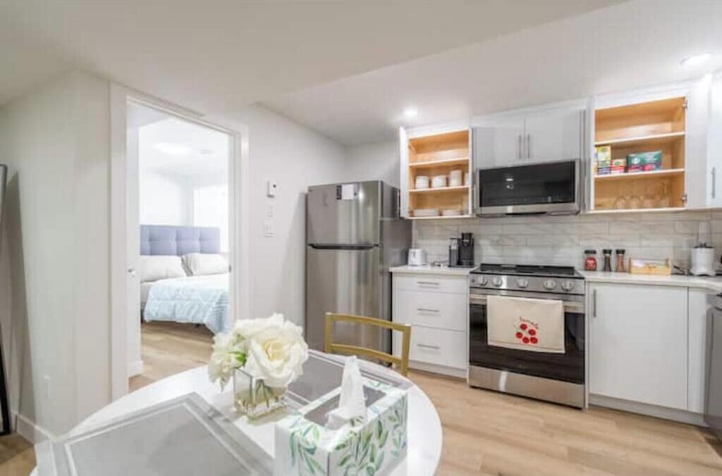 A modern kitchen with stainless steel appliances, white cabinetry, and a dining area with a table and chairs.
