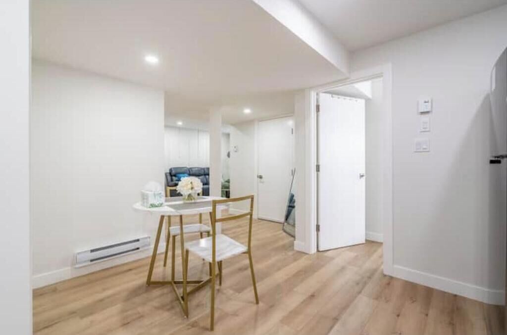 Un intérieur moderne comprenant un coin repas avec une table et des chaises, un couloir menant à une autre pièce, et une porte dotée d’un interrupteur.