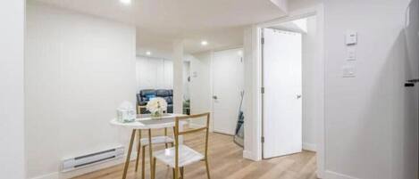 Un intérieur moderne comprenant un coin repas avec une table et des chaises, un couloir menant à une autre pièce, et une porte dotée d’un interrupteur.