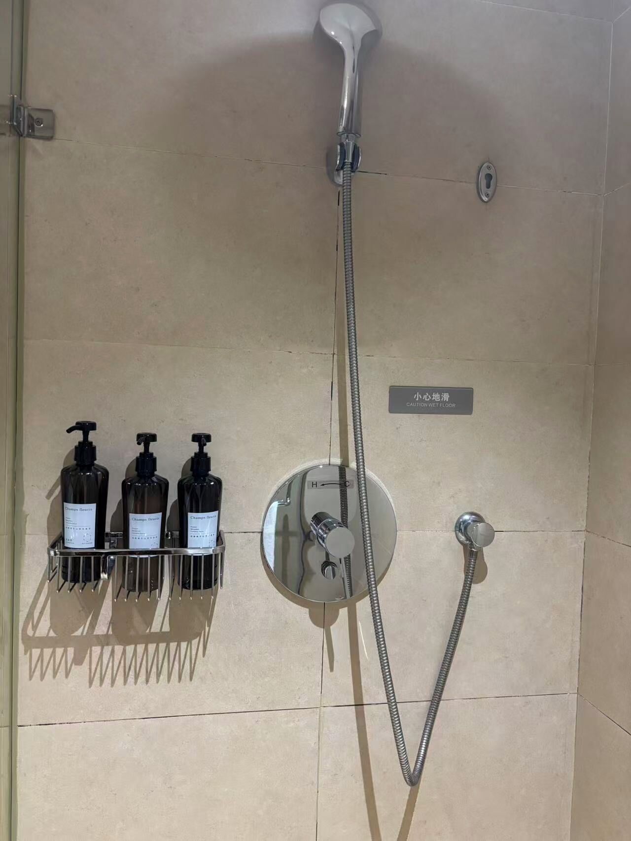 A shower with a handheld showerhead, a wall-mounted control panel, and three bottles of shampoo.
