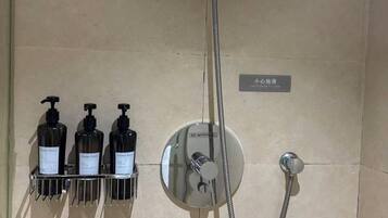 A shower with a handheld showerhead, a wall-mounted control panel, and three bottles of shampoo.