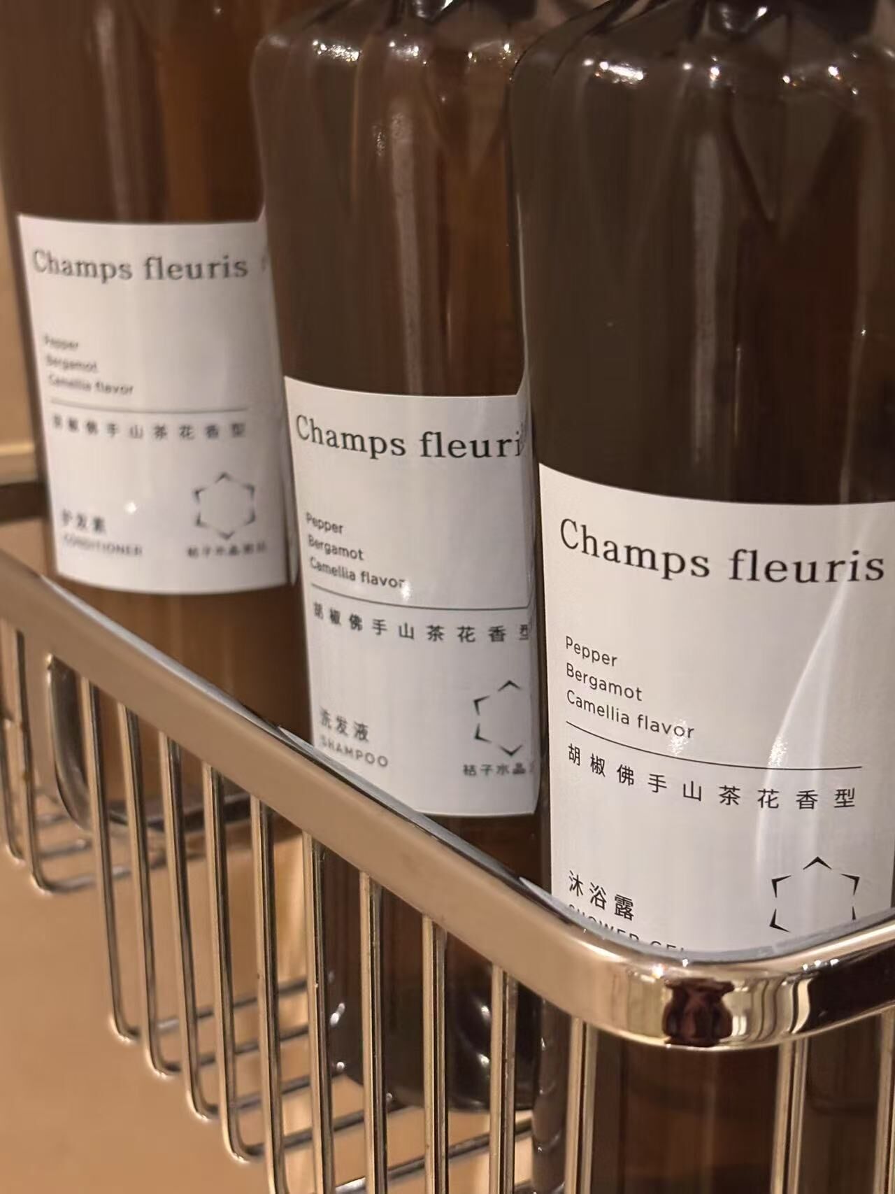 A shelf with bottles of shampoo labeled 'Champs fleuris' with a 'Pepper Bergamot Camellia flavor'.