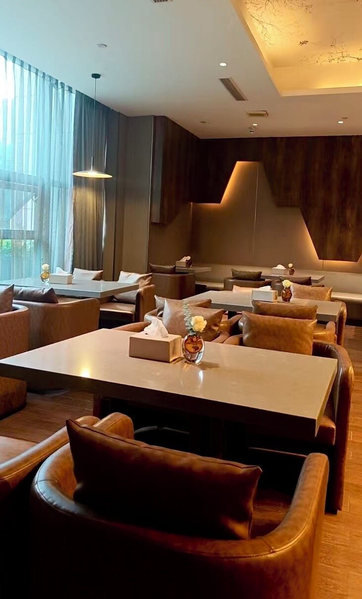 A modern restaurant with leather seating, tables, and a warm ceiling design.
