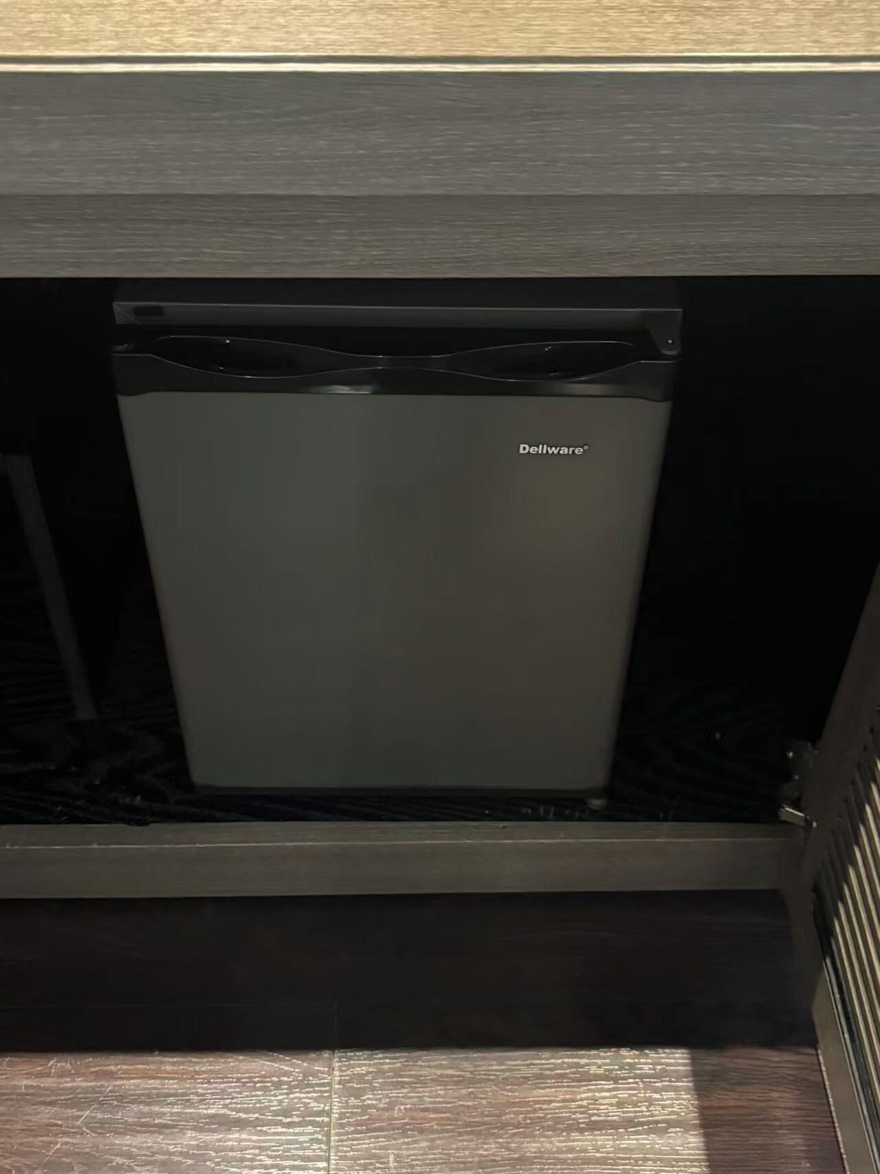 A compact refrigerator with a metallic finish, located under a wooden cabinet.