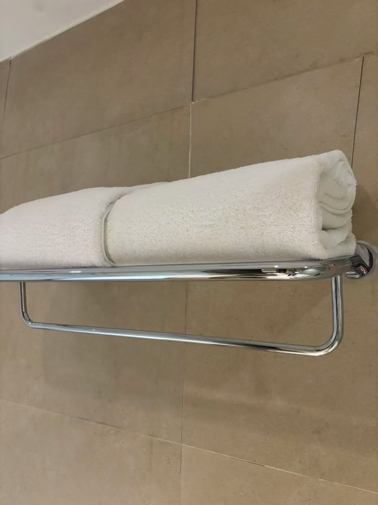 Una toalla blanca enrollada sobre un perchero de cromo frente a una pared de azulejos.