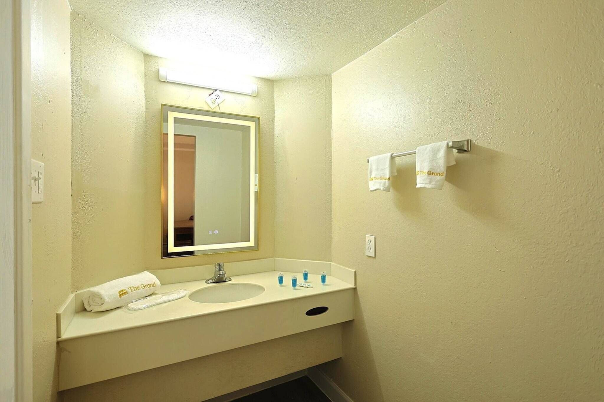 Une salle de bain équipée d’un lavabo, d’un miroir, d’un porte-serviettes et d’une petite serviette ornée de l’inscription « The Grand ».