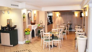Un hall de hotel con un mostrador de recepción, varias mesas de comedor con sillas, una chimenea y una zona de cocina al fondo.