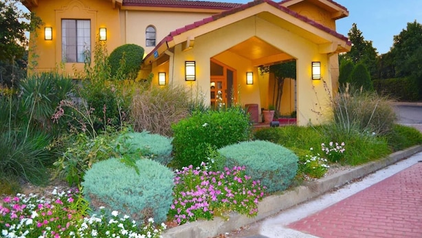Una casa amarilla con un porche, rodeada de jardines cuidados y un sendero de ladrillos.