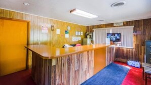 A room with a wooden reception desk, a television, and a window with blinds.