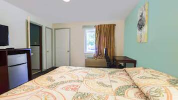 A bedroom with a bed, a desk, a chair, a television, and a door.