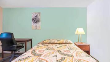 A hotel room with a bed, a desk, a chair, a lamp, and a painting on the wall.