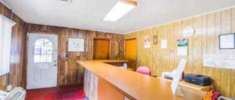 A reception area with a wooden interior, a reception desk, a white chair, a blue carpet, and a door.