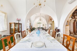 Ein Esszimmer mit einem langen Tisch, gedeckt für eine Mahlzeit, mit gewölbten Decken und einem Kronleuchter.
