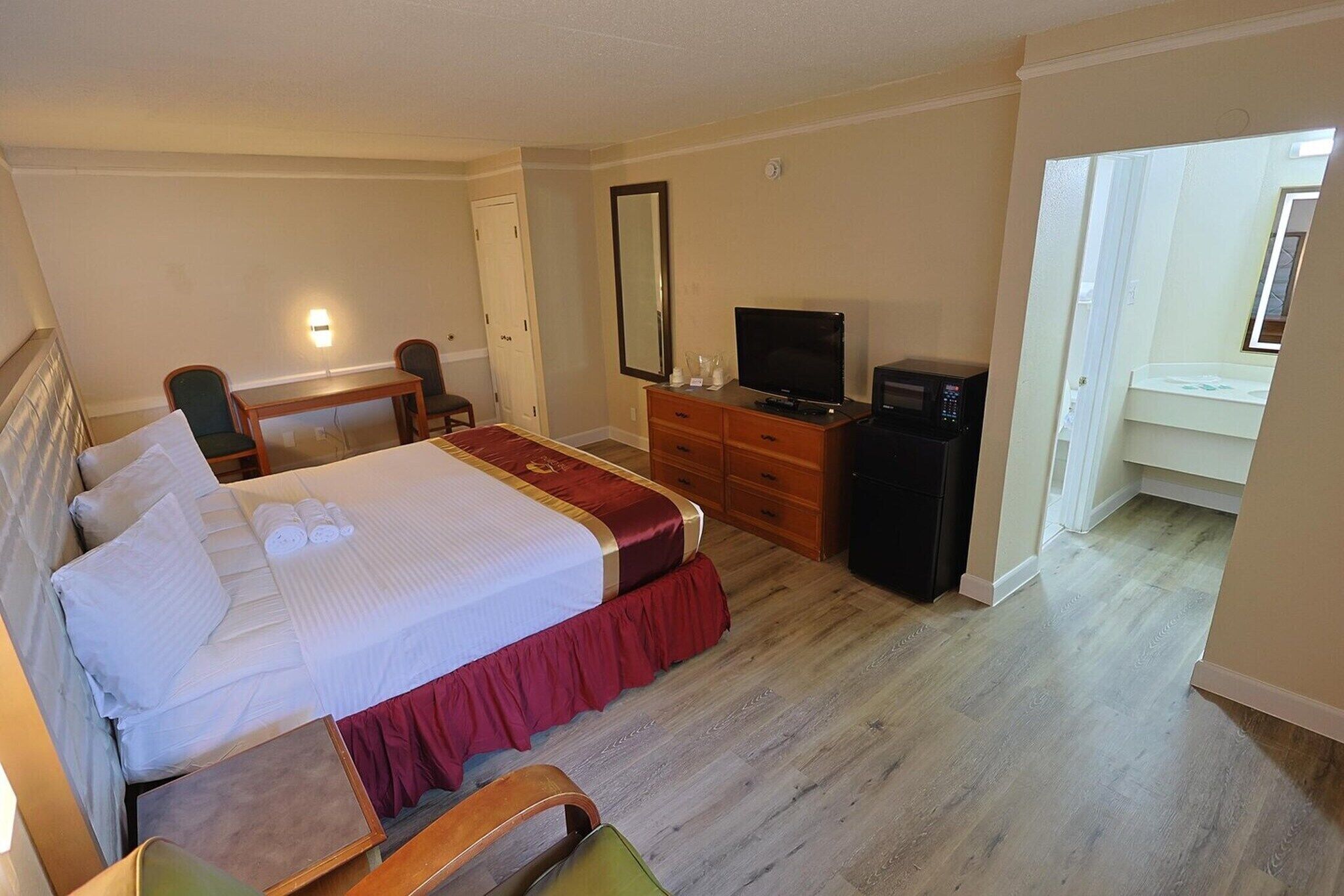 Hotellihuone, jossa on sänky, työpöytä, televisio ja peili.