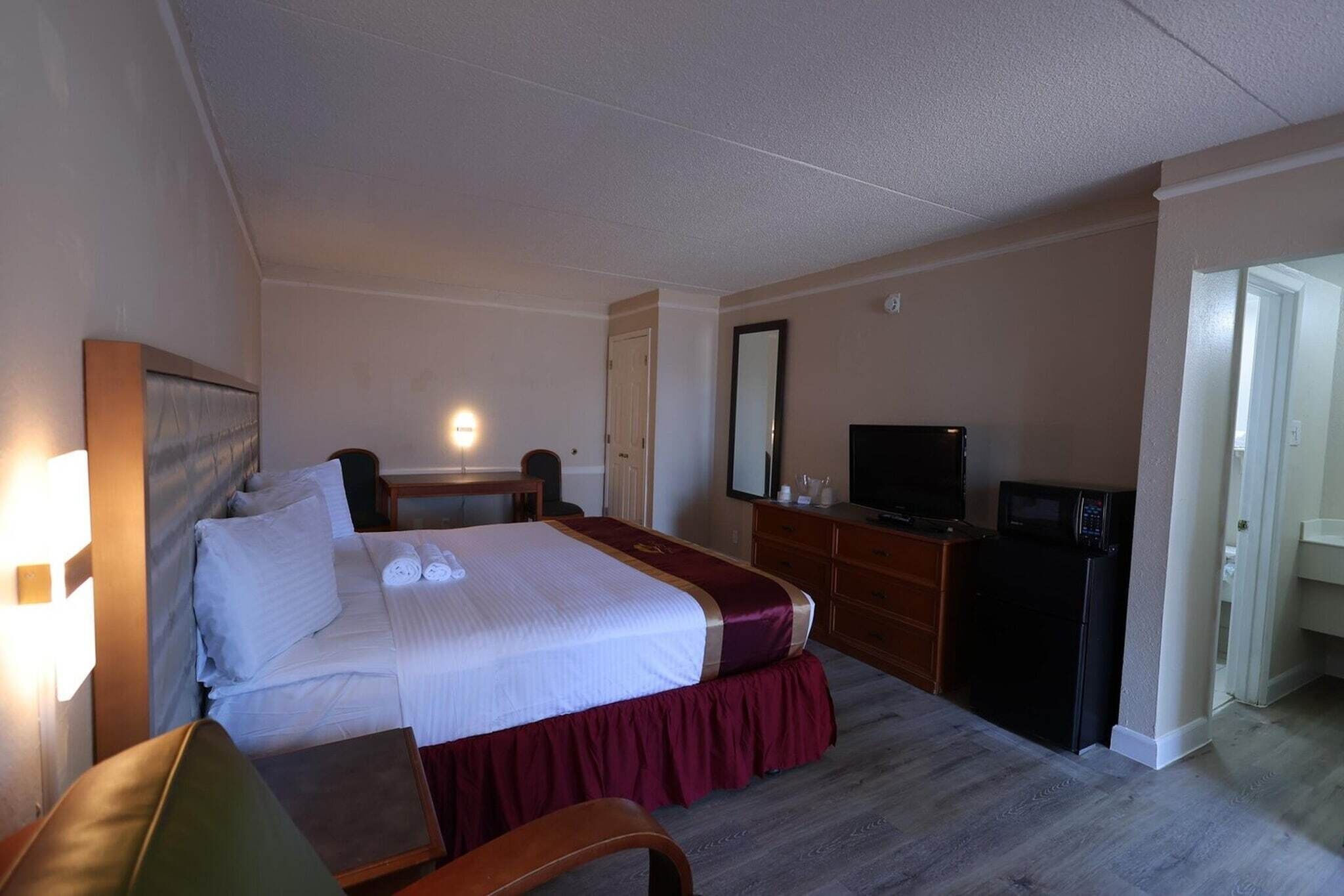 A hotel room with a bed, a desk, a television, a refrigerator, and a mirror.