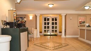 A hotel lobby with a reception desk, a waiting area with chairs, a tiled floor, and a door leading to another room.