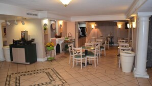 A dining area with a round table and chairs, a kitchen in the background, and a patterned rug on the floor.