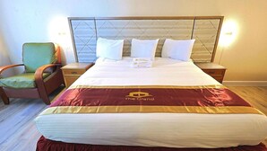 A hotel room with a large bed, a nightstand, a green chair, and a headboard with a diamond pattern.