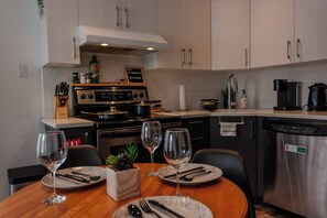 A modern kitchen with a stove, sink, and dishwasher. There are two dining tables with wine glasses and cutlery. - Bright Home with Balcony - 15 min to Premium Outlets (Mirabel)