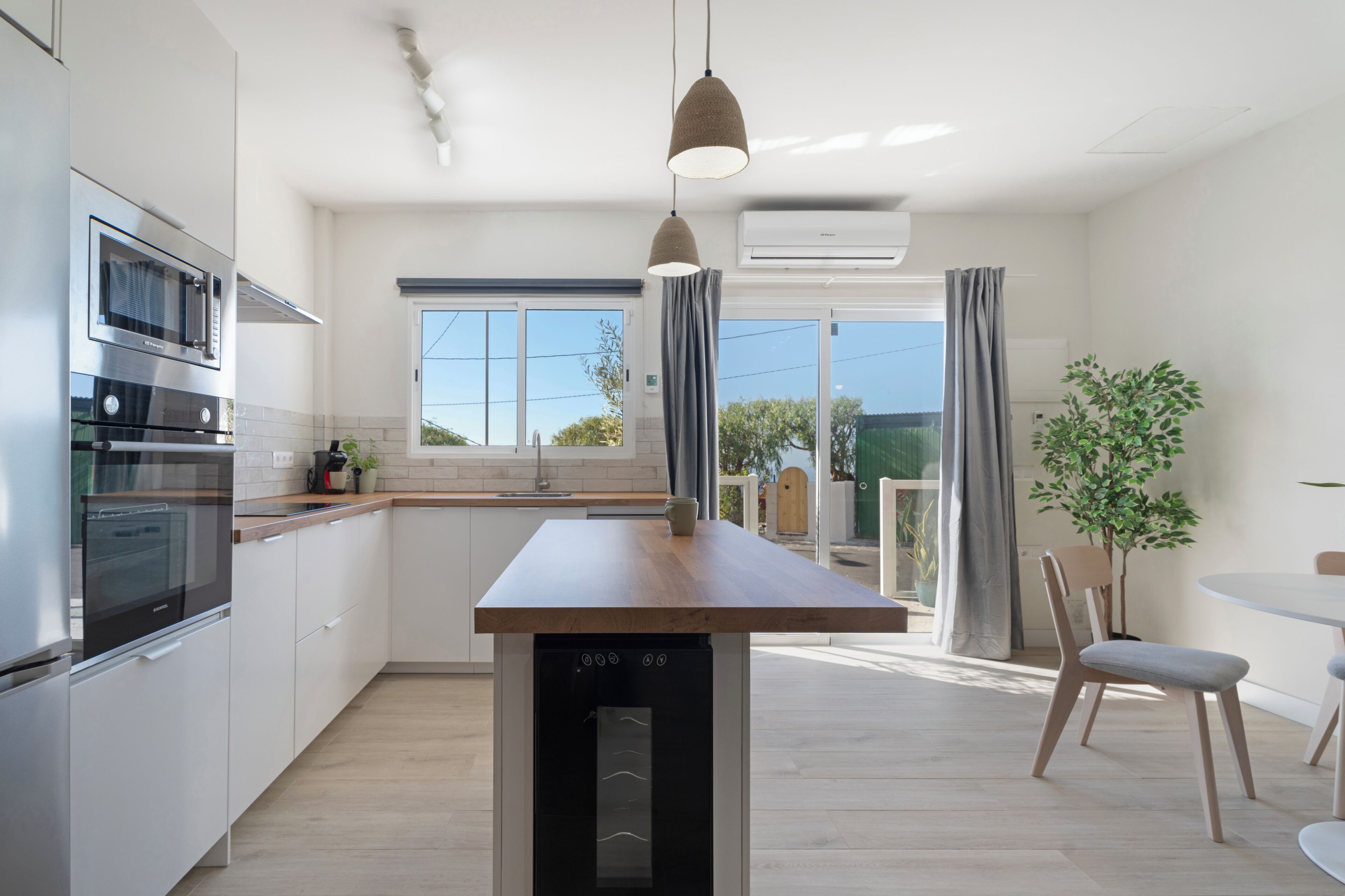 Une cuisine moderne dotée d’appareils électroménagers intégrés, un coin repas avec une table et des chaises, et une vue sur l’extérieur.