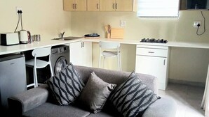 A compact living space with a kitchenette, a sofa with patterned cushions, and a small dining area. - The Corner Nest at Constantia Kloof with backup Wi-Fi (Roodepoort)