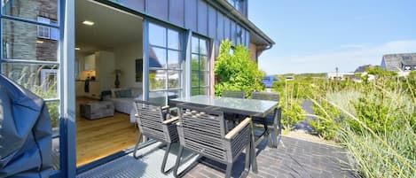 A modern house with a patio, a dining area with chairs, and a view of the surrounding landscape.