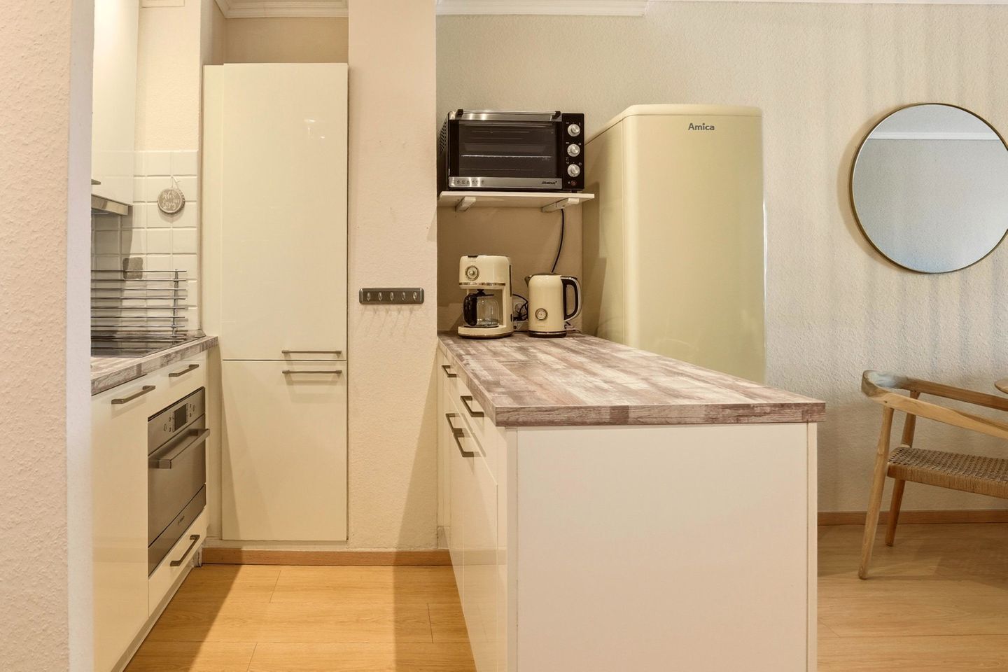 A compact kitchen with a microwave, coffee maker, and toaster, a small refrigerator, and a wooden bench.