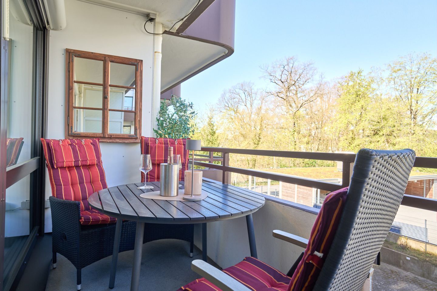 A balcony with a round table, two chairs, a metal container, and a candle.