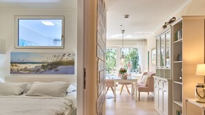 A bedroom with a bed, a painting of a beach, and a view of the outdoors through a window. - Arrive, take a deep breath, enjoy—Apartment LichtSpiel - Residenz am Hang (Scharbeutz)