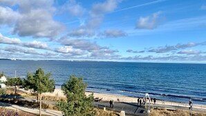 A coastal view with a clear sky, a beach, and a boardwalk with people walking. - Arrive, take a deep breath, enjoy—Apartment LichtSpiel - Residenz am Hang (Scharbeutz)