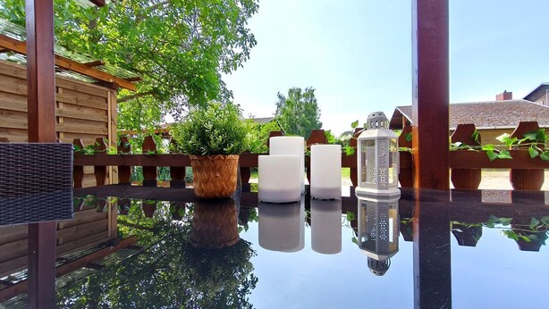 Un patio con tavolo in vetro, piante in vaso e mobili da esterno.