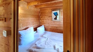 Una camera da letto in legno con un letto, cuscini, un quadro appeso alla parete e un interruttore della luce.