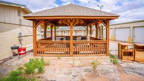 A wooden gazebo with a roof, surrounded by a gravel area, and adjacent to a building with a garage. - 2 Queen Bed | Smoking (Snyder TX)