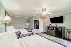 Een hotelkamer met twee bedden, een plafondventilator, een televisie, een minibar en een badkamer.