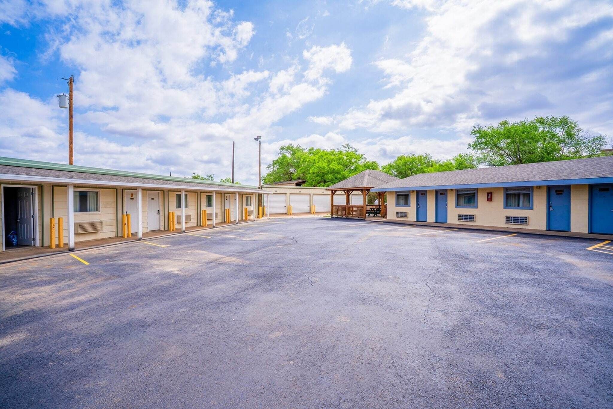 A motel with a central parking lot, individual rooms with doors, and a covered outdoor seating area.