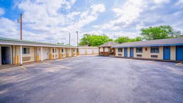 A motel with a central parking lot, individual rooms with doors, and a covered outdoor seating area.