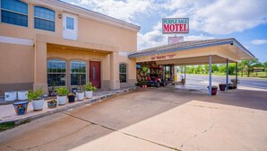A motel with a covered parking area, a sign indicating 'No Trucks,' and potted plants along the sidewalk. - 2 Queen Bed | Smoking (Snyder TX)