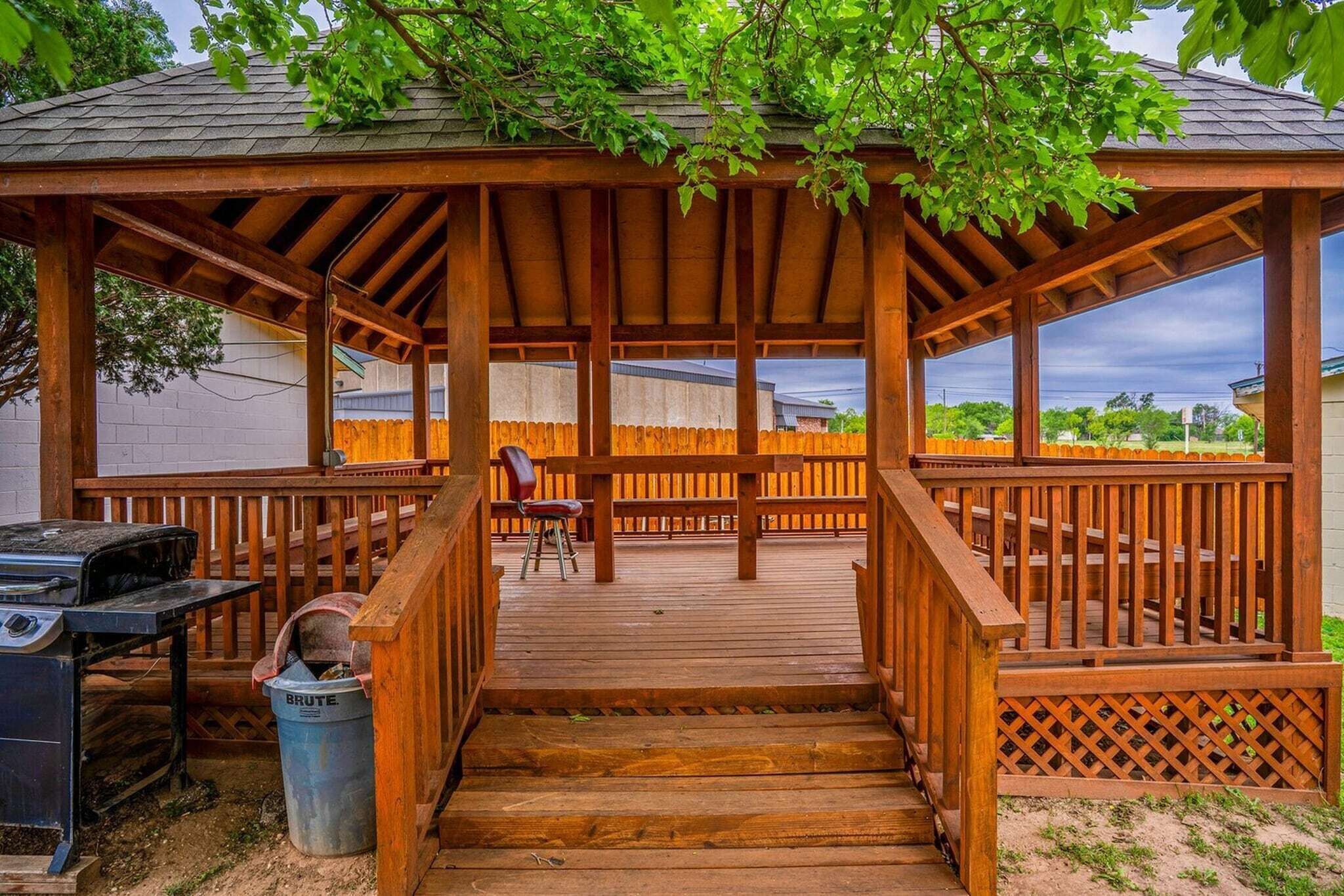 A wooden deck with a pergola, a grill, and a trash can.
