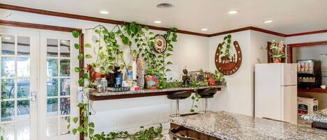A kitchen with a marble countertop, a refrigerator, and a dining area with chairs.