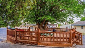 A wooden deck with a fence, a large tree, and a building in the background. - 2 Queen Bed | Smoking (Snyder TX)