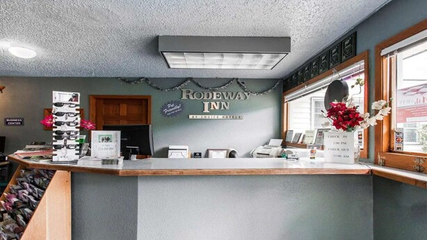 A reception desk with a sign for Rodeway Inn, a business center, and a window with a view.