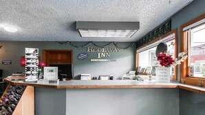A reception desk at Rodeway Inn with a sign above it, a window with flowers, and a counter with various items. - Full Bed Non-Smoking (Stevenson WA)