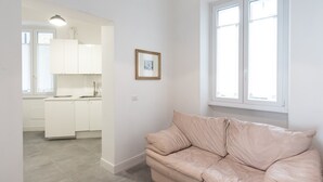Un interior moderno con un sofá de cuero color beige, una cocina con armarios blancos y un cuadro en la pared.