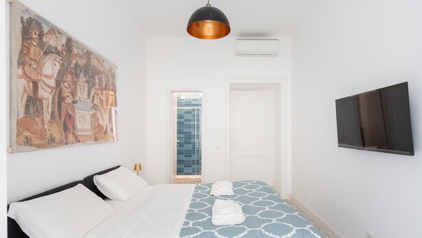 Una habitación de hotel con una cama, un cuadro, un televisor y una puerta.