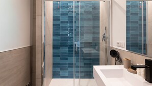 Un baño moderno con ducha de vidrio, lavamanos blanco y espejo sobre él.