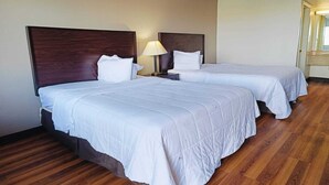 A hotel room with two beds, wooden flooring, and a nightstand with a lamp.