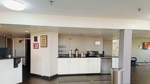 A modern kitchen with white cabinets, a microwave, and a sink. There are framed certificates on the wall and a trash can in the corner.