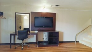 A room with a wooden floor, a desk with a chair, a mounted TV, and a staircase.